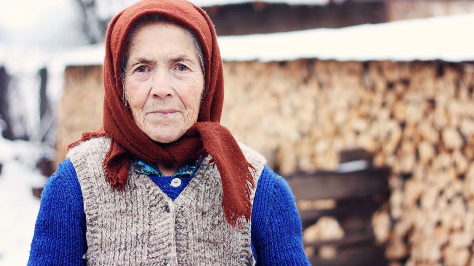 An elderly Slavic woman stands outside in the snow.