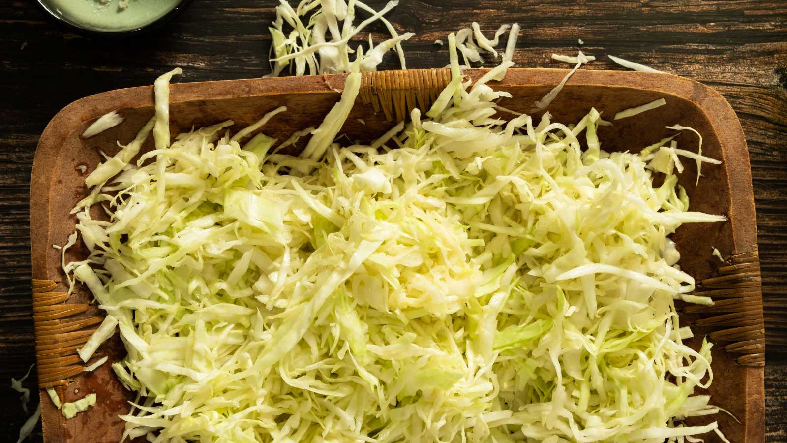 Shredded and salted green cabbage sitting in a wooden bowl.