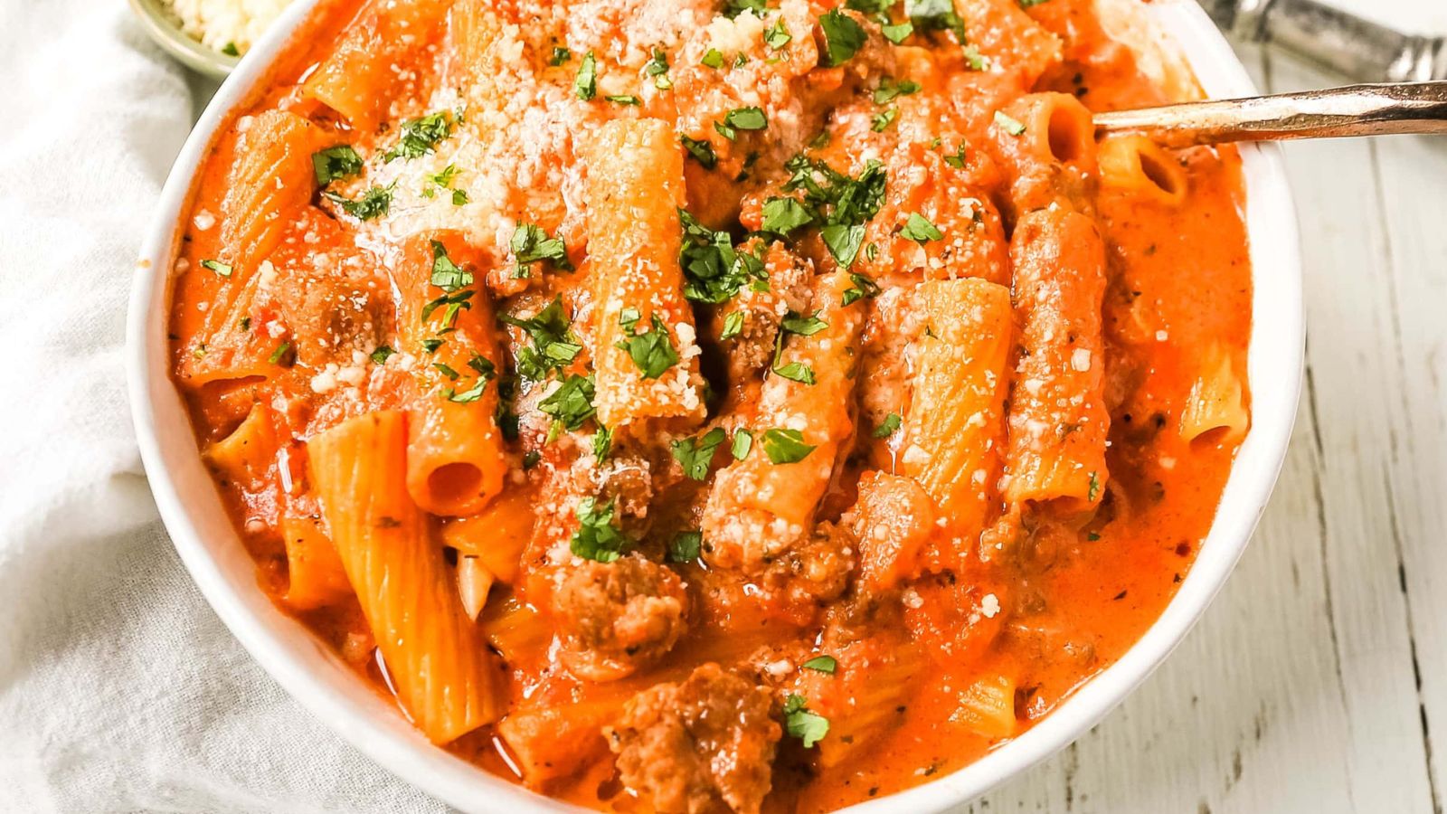 A bowl of creamy sausage rigatoni pasta with extra parm and fresh basil on top of it.