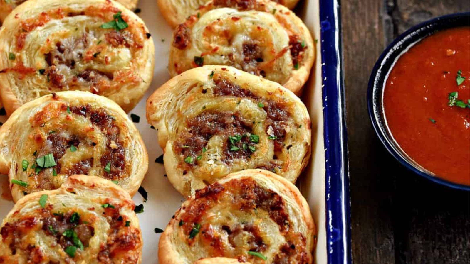 Puff pastry sausage pinwheels served with pizza sauce on a plate.