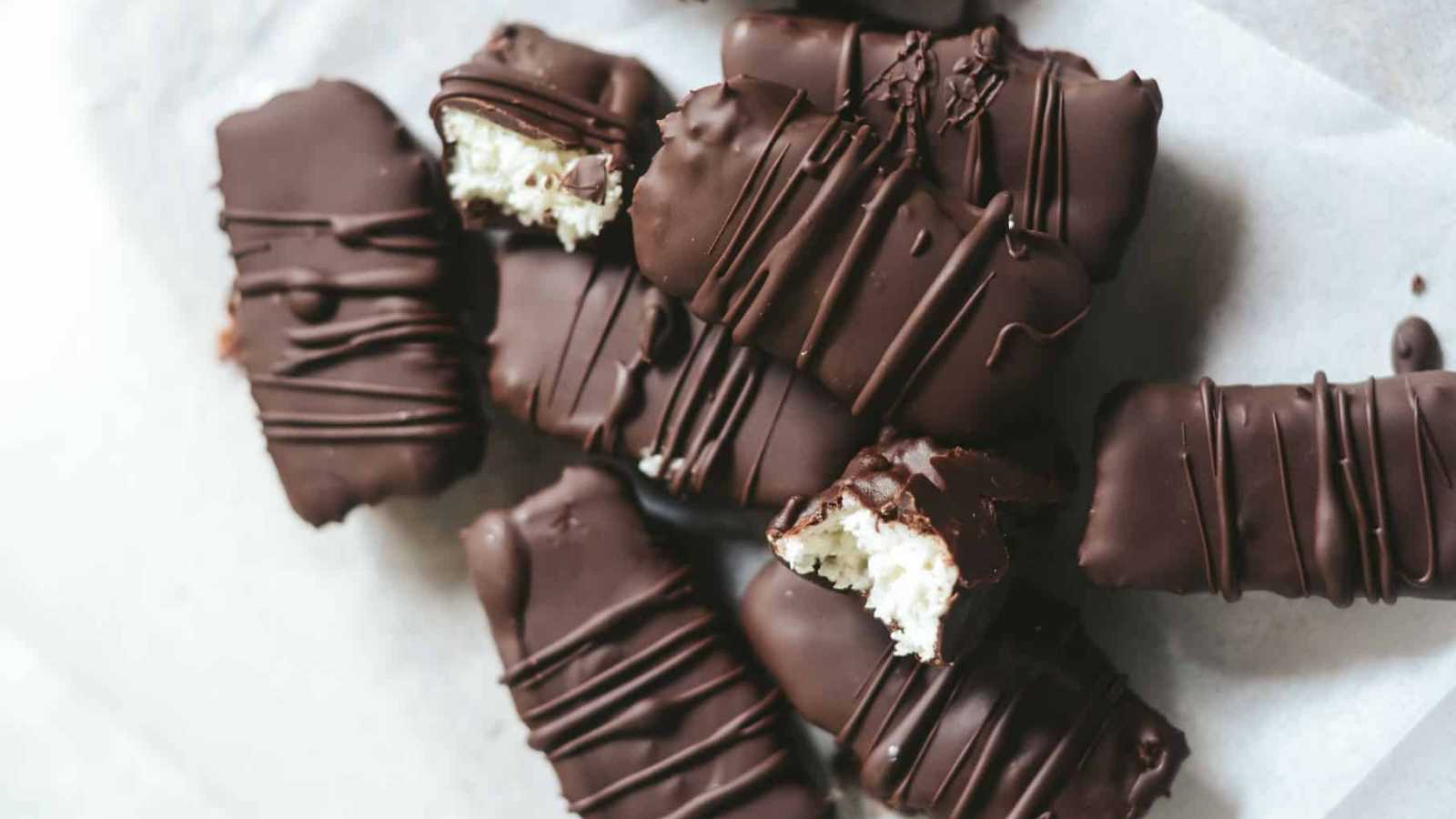 Creamy coconut bars covered with chocolate in white paper tissue.