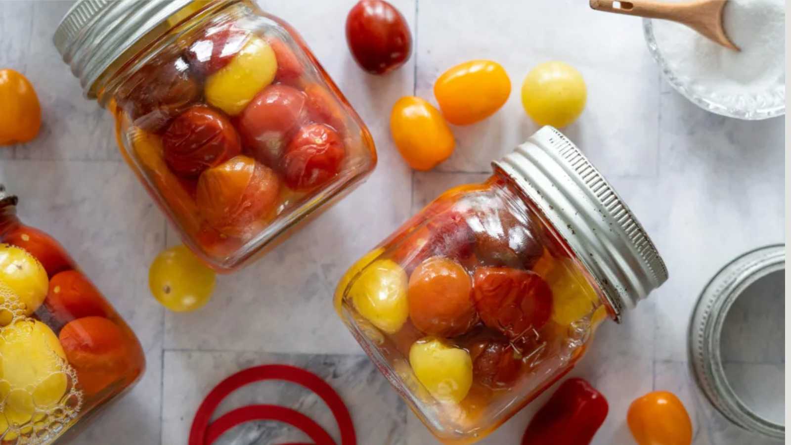 A jar of cherry tomatoes with raw tomatoes and salt beside.