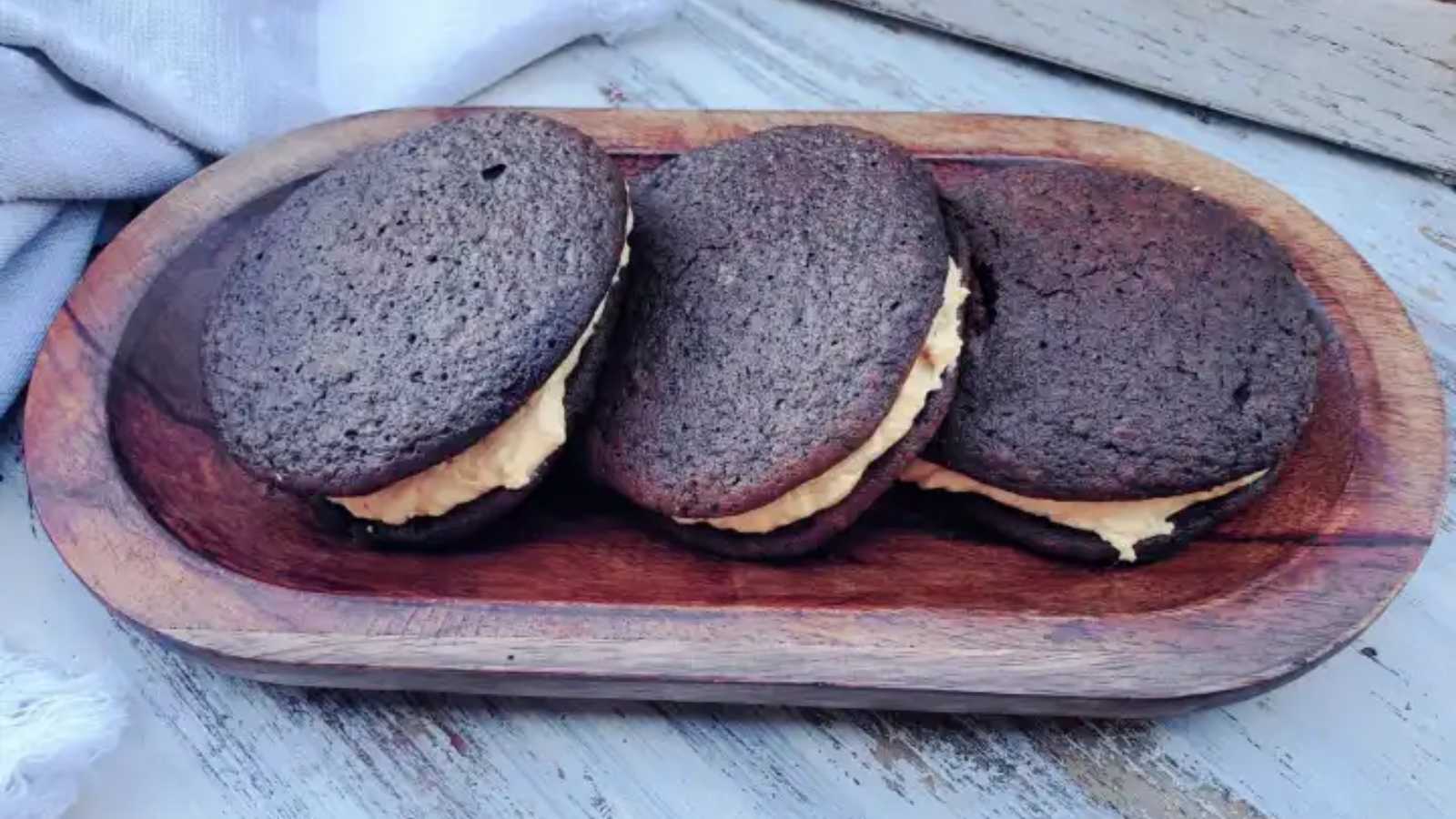 A chocolate whoopie pie is on the top of a wooden bowl.