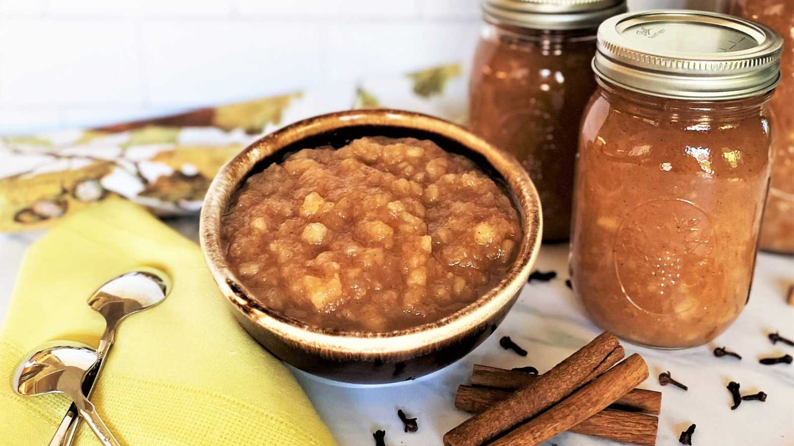 A bowl and jars of homemade applesauce with 2 spoon beside.