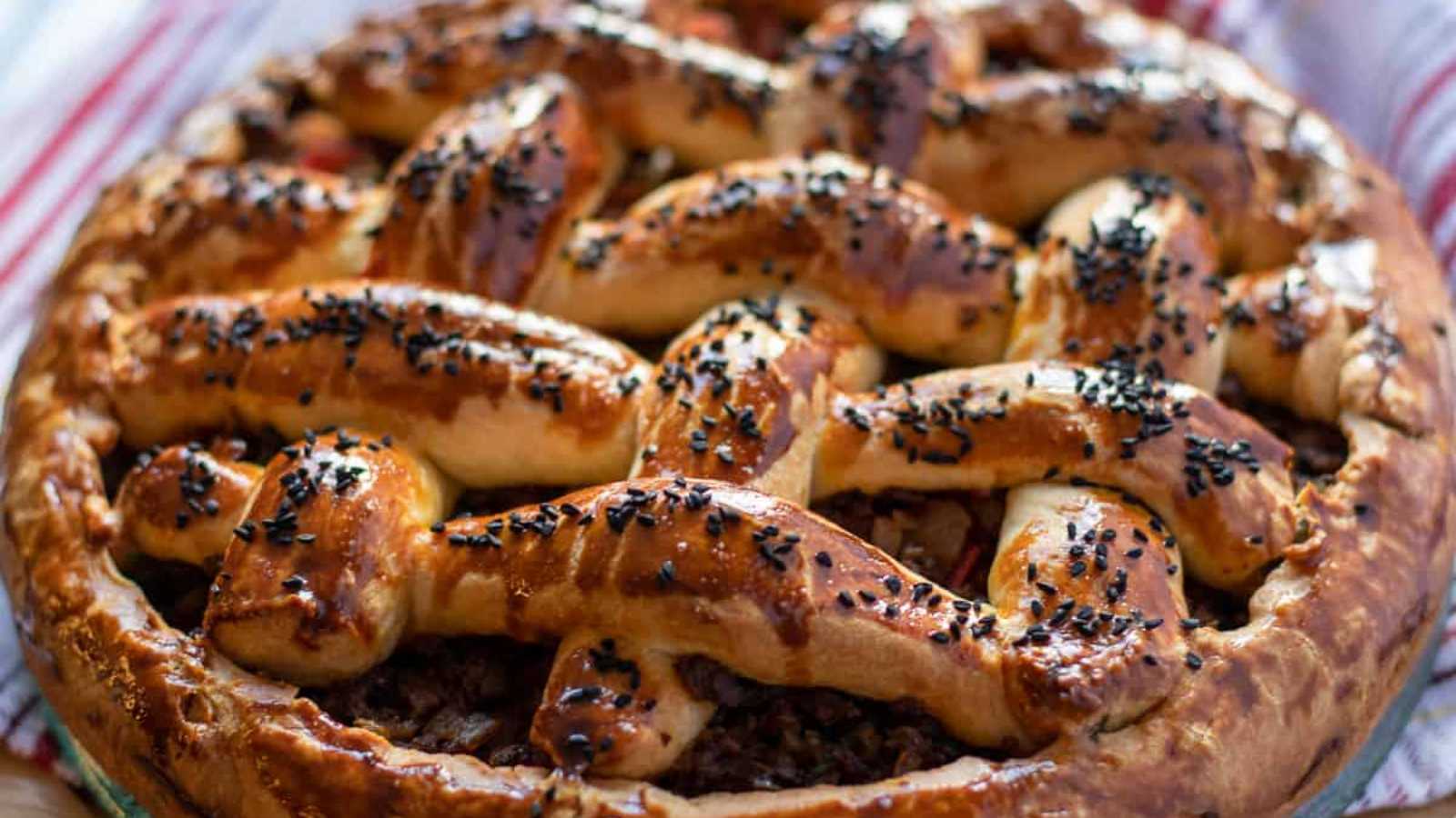 A whole beef pie adorned with a sprinkle of black sesame seeds.