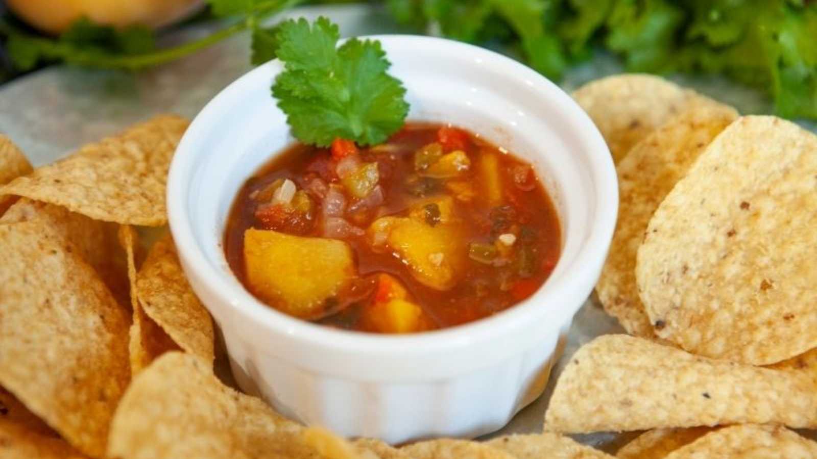 A bowl of peach salsa with crackers around.