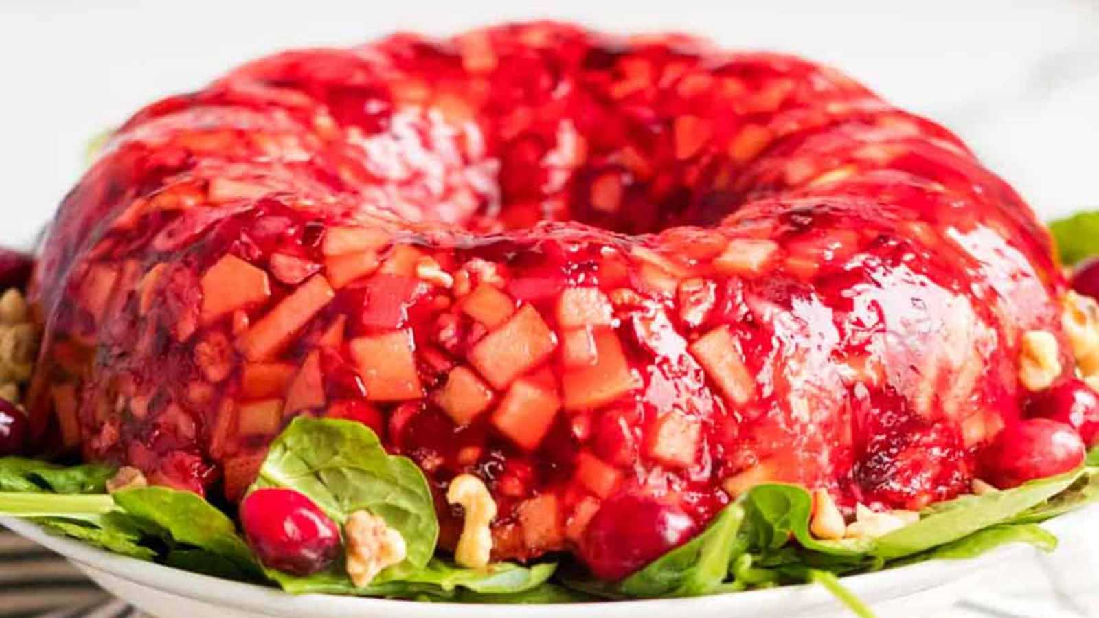 A red cranberry jello salad with fresh fruit in a bundy-type mold on a platter for serving.