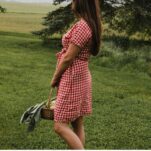 A woman in a red gingham wrap dress holds a basket of fresh vegetables on her homestead.