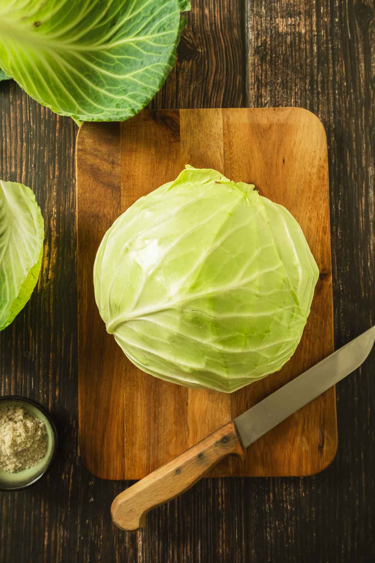 A large green cabbage head with the outer leaves removed sitting on a wooden cutting board.