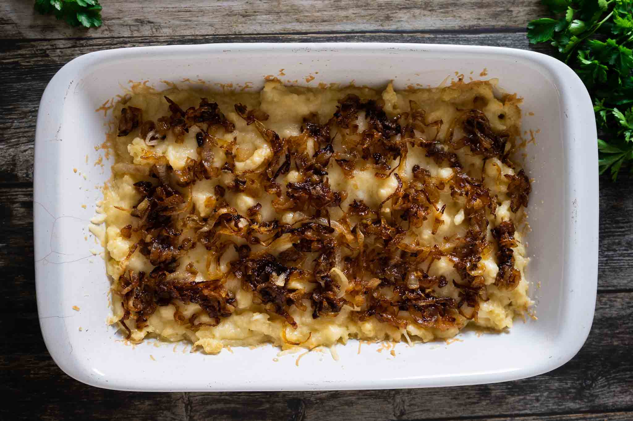 A casserole dish full of cheesy spaetzle, with caramelized onions added on top.