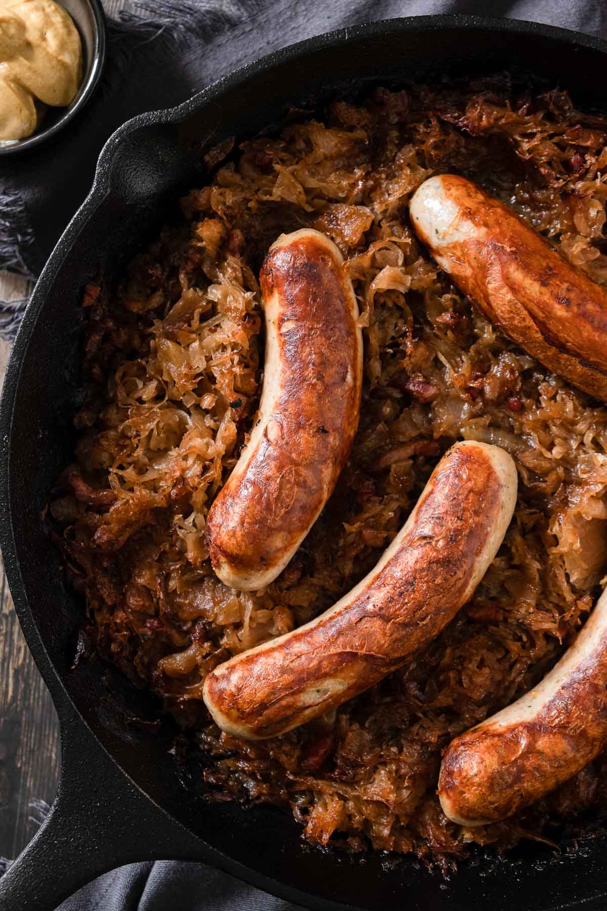 Golden brown bratwurst sausages nestled in braised sauerkraut in a cast iron skillet.