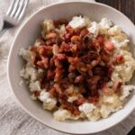 A bowl of creamy bryndzové halušky topped with caramelized onions and bacon.