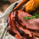 Three slices of oven-baked glazed ham served with roasted potatoes, carrots, and other root veggies.