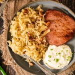 German kassler chop served on a plate next to braised sauerkraut and a creamy horseradish sauce.