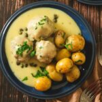 German Königsberger Klopse meatballs in a creamy lemon and caper sauce served on a blue plate.