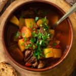 A bowl full of authentic Hungarian goulash full of thick red sauce, tender chunks of beef, potatoes and more.