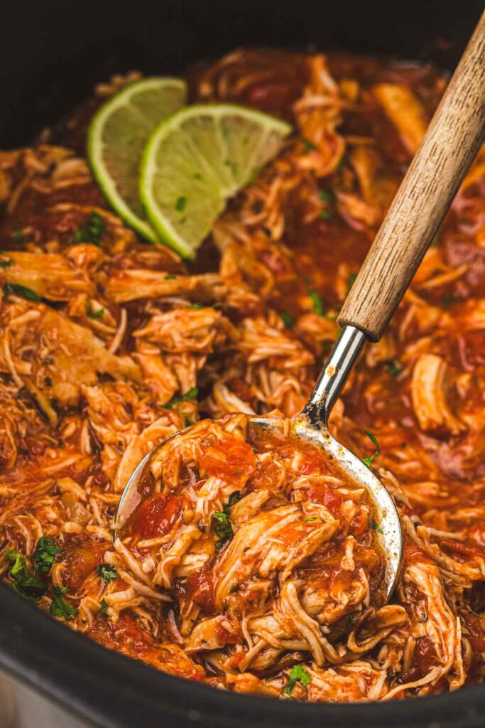 The finished and shredded salsa chicken being stirred inside slow cooker.