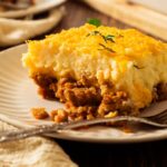 A big, thick slice of cowboy meatloaf and potato casserole topped with melted cheese on a white plate.