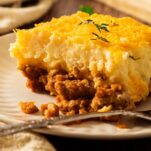 A big, thick slice of cowboy meatloaf and potato casserole topped with melted cheese on a white plate.