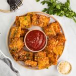 Fried ravioli served on a plate with a bowl of marinara sauce for dipping.