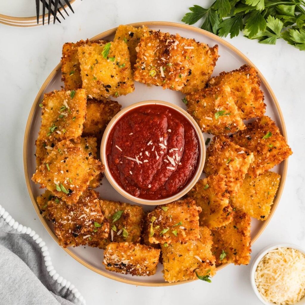 Fried ravioli served on a plate with a bowl of marinara sauce for dipping.