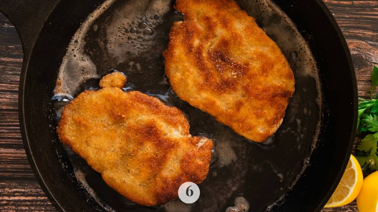 The pork schnitzel being fried to a golden brown crispiness in a cast iron skillet and hot lard.