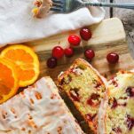 A glazed loaf of sourdough orange cranberry quick bread on a wooden platter, cut into thick slices.
