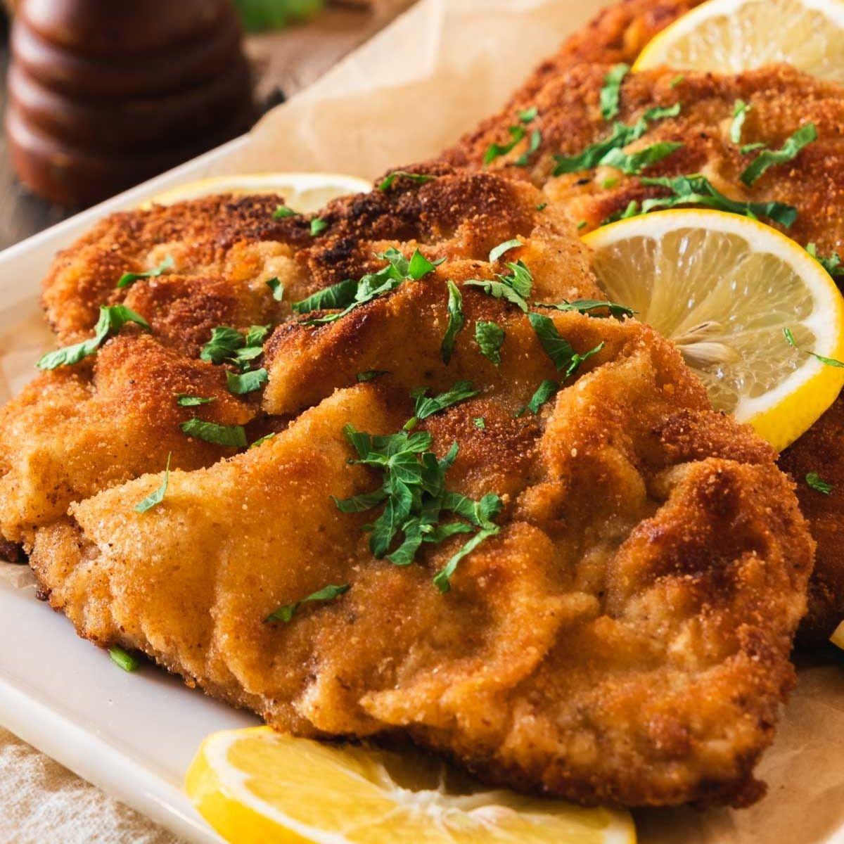 German schnitzel arranged on a platter for serving with fresh lemon wedges and parsley.