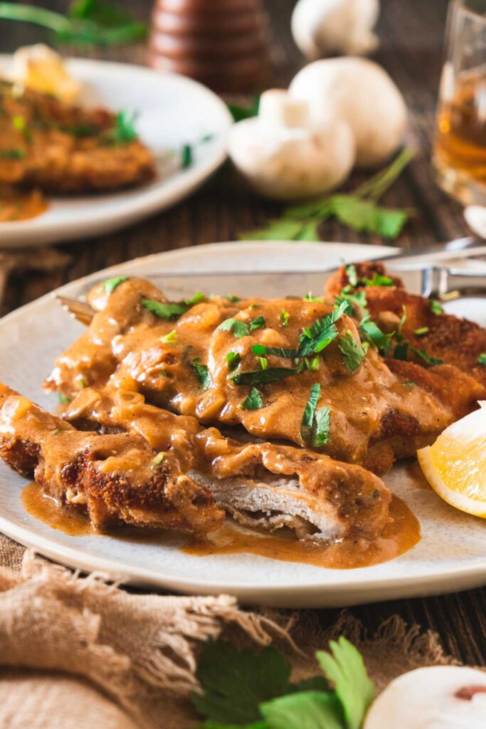 Crispy schnitzel covered in a rich and creamy mushroom gravy served on a plate.