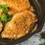 Two pieces of finished Longhorn parmesan crusted chicken inside of a cast iron skillet. The parmesan crust os golden brown.