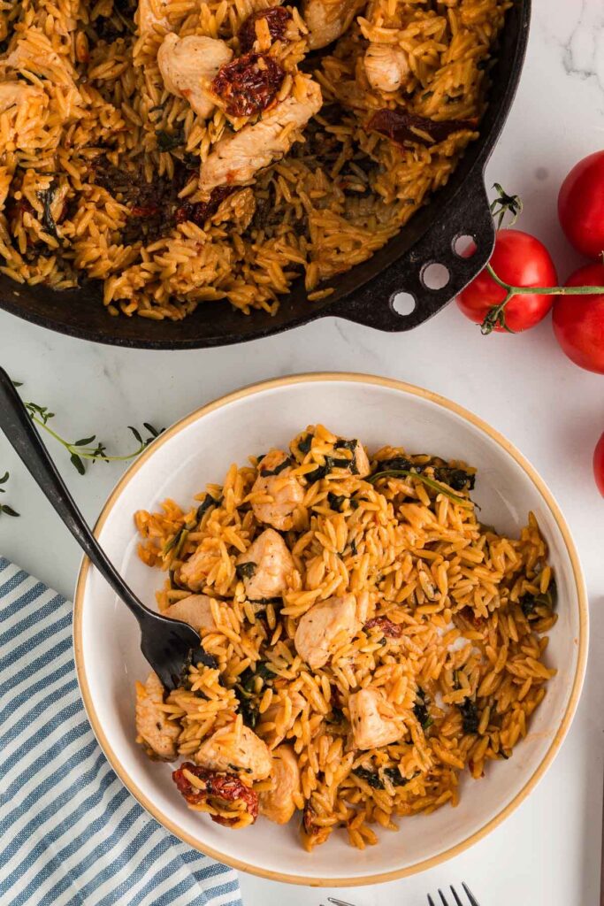 A pot and bowl full of creamy marry me chicken orzo pasta with spinach and sundried tomatoes.