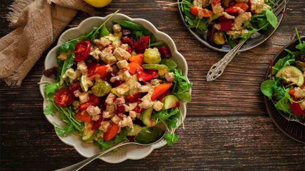 A colorful salad full of lettuce, greens, and roasted vegetables.