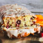 A glazed loaf of sourdough orange cranberry quick bread on a wooden platter.