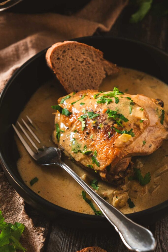 A chicken thigh with golden crispy skin in a thick and creamy deep yellow mustard sauce.