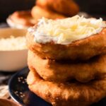 A stack of Hungarian fried bread lángos with sour cream and shredded cheese.