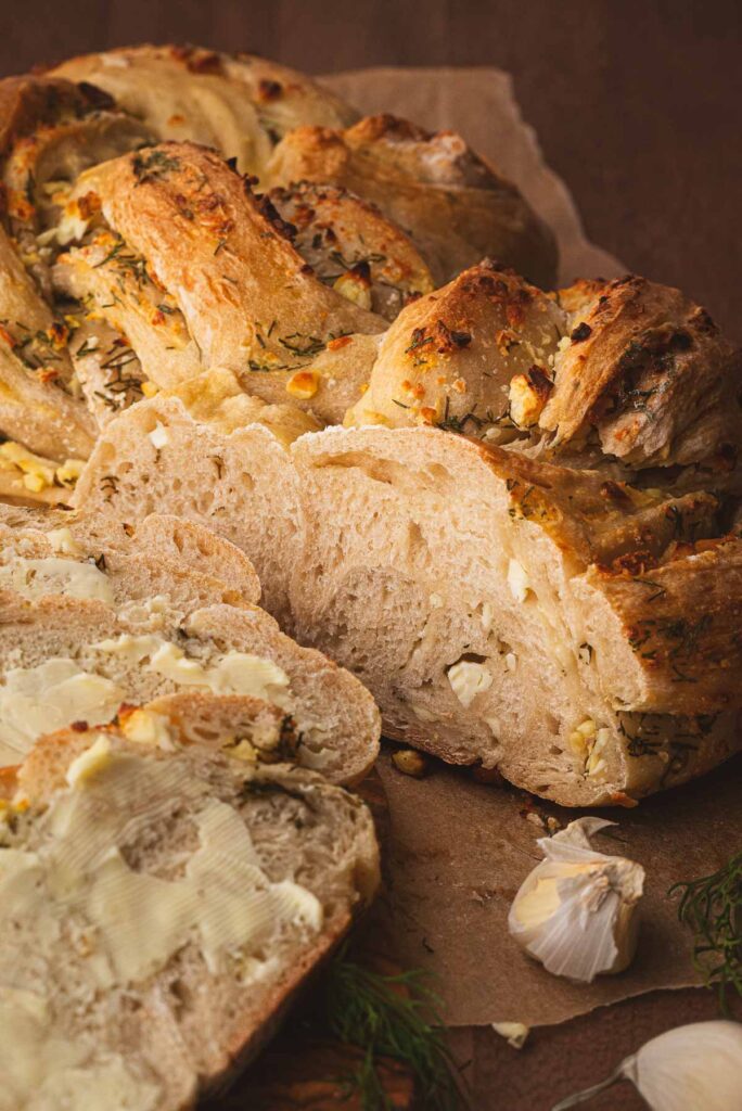 A loaf of twisted sourdough bread with dill and feta sliced open on cutting board.