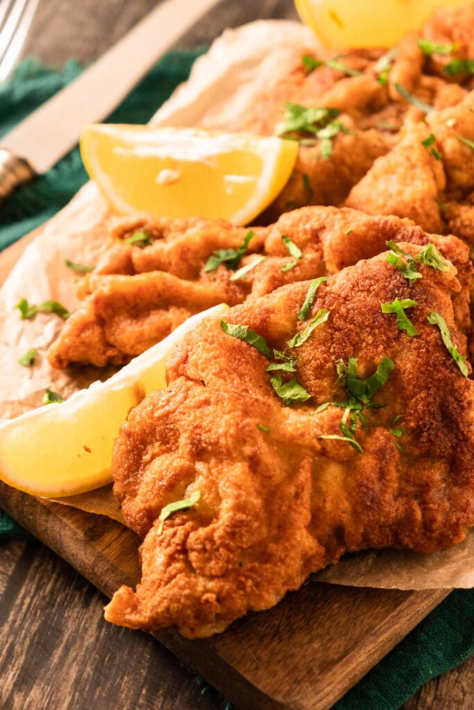 A platter of golden, crispy, fried wienerschnitzel. Lemon wedges are on the side.