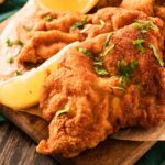 A platter of golden, crispy, fried wienerschnitzel. Lemon wedges are on the side.
