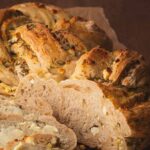 A loaf of twisted sourdough bread with dill and feta sliced open on cutting board.