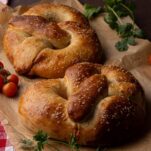 Two golden-brown pizza-stuffed sourdough pretzels placed on parchment with cherry tomatoes and herbs.