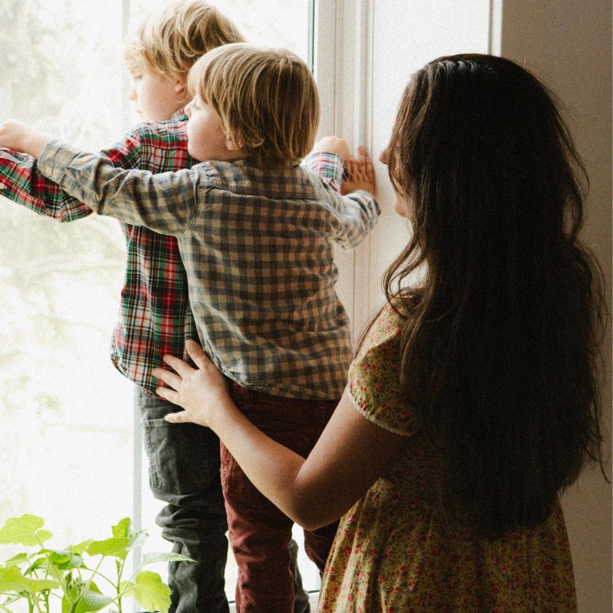 A woman with her sons at the window sill.