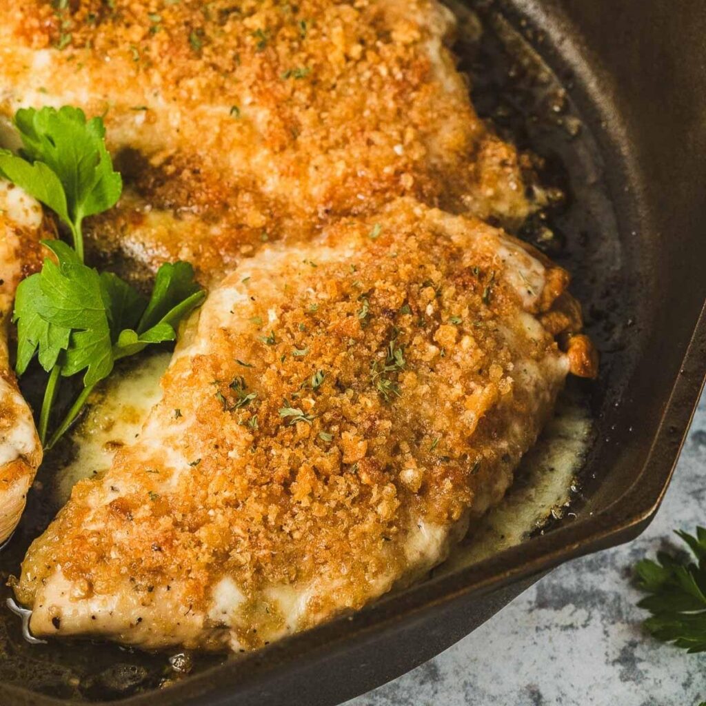 Two pieces of finished Longhorn parmesan crusted chicken inside of a cast iron skillet. The parmesan crust os golden brown.