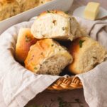 A basket of pillowy soft sourdough pull apart dinner rolls covered in a butter sauce infused with herbs.