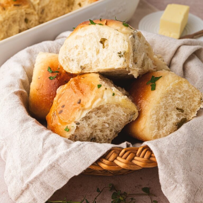 A basket of pillowy soft sourdough pull apart dinner rolls covered in a butter sauce infused with herbs.