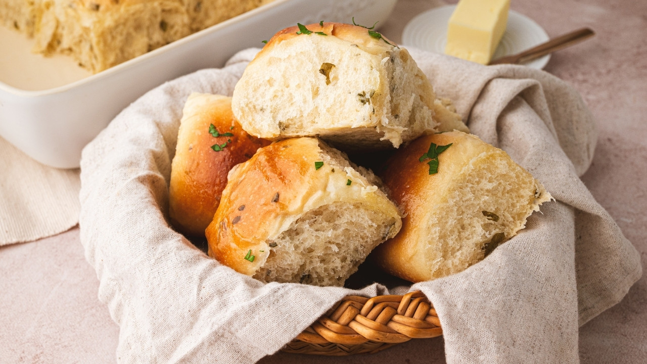 A basket of pillowy soft sourdough pull apart dinner rolls covered in a butter sauce infused with herbs.
