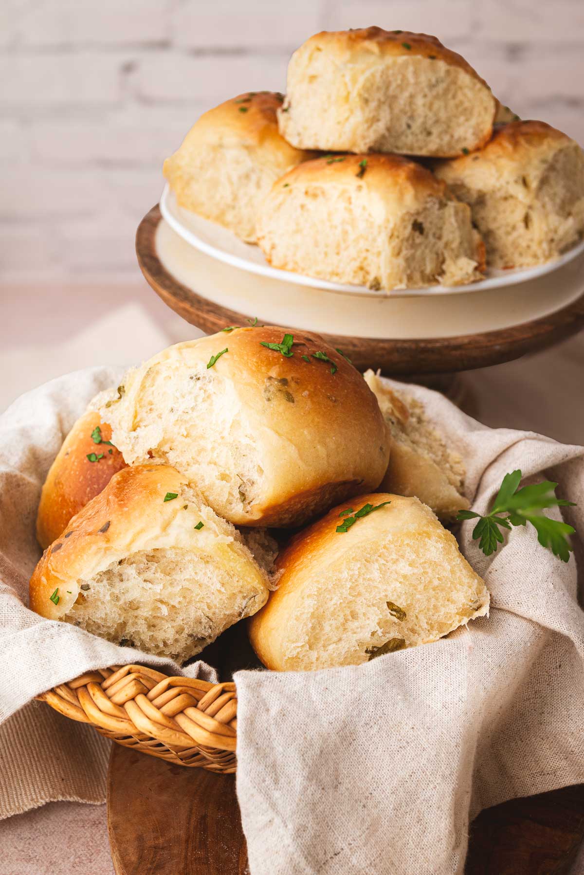 A basket and platter of pillowy soft sourdough pull apart dinner rolls covered in a butter sauce infused with herbs.