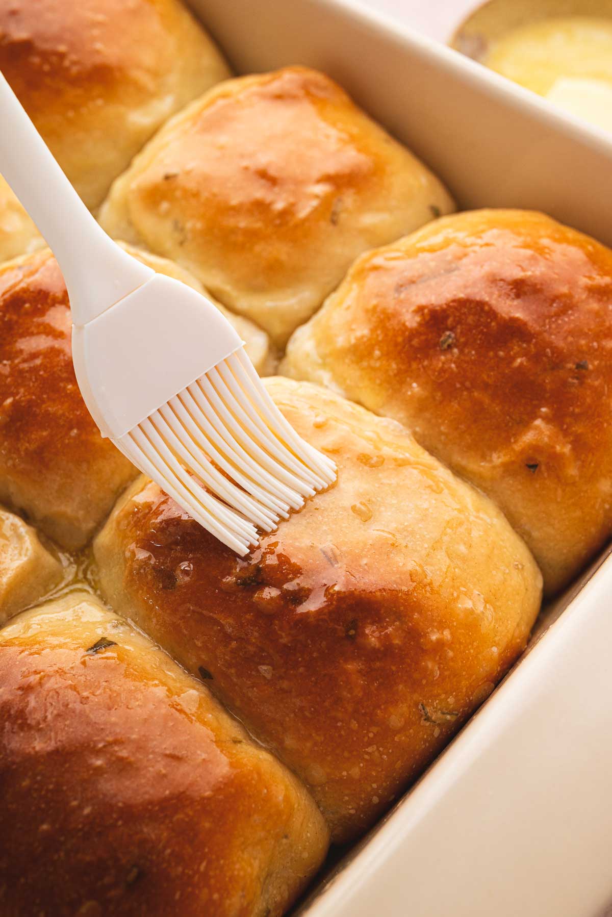 Sourdough slider buns baked in a tray being covered in butter.
