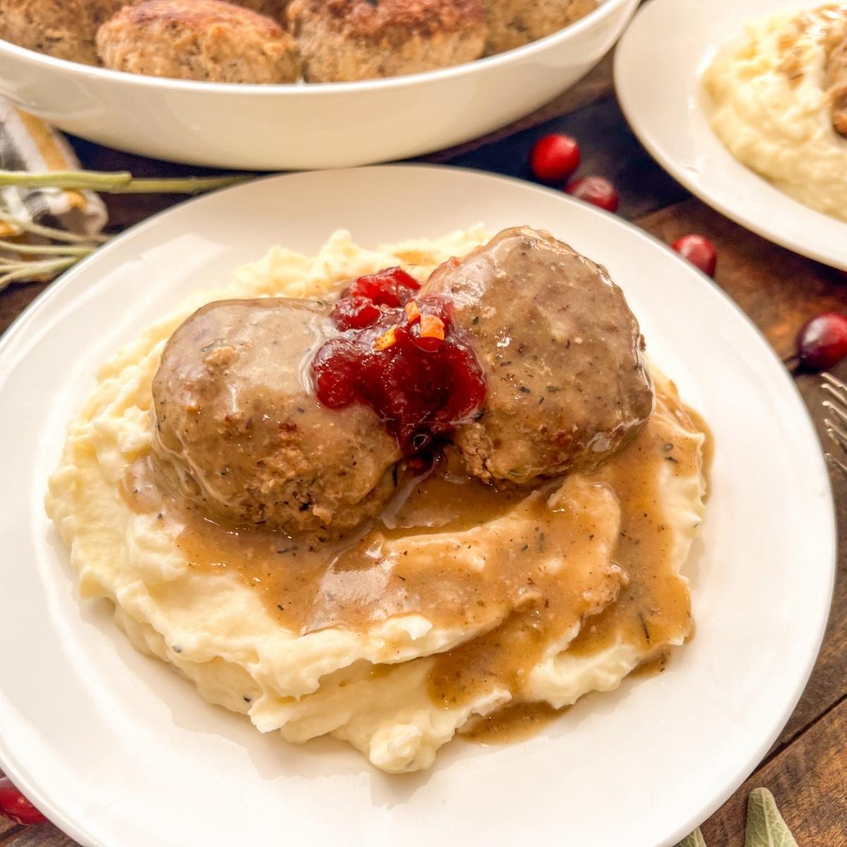Turkey meatballs covered in gravy and cranberry sauce on mashed potatoes.