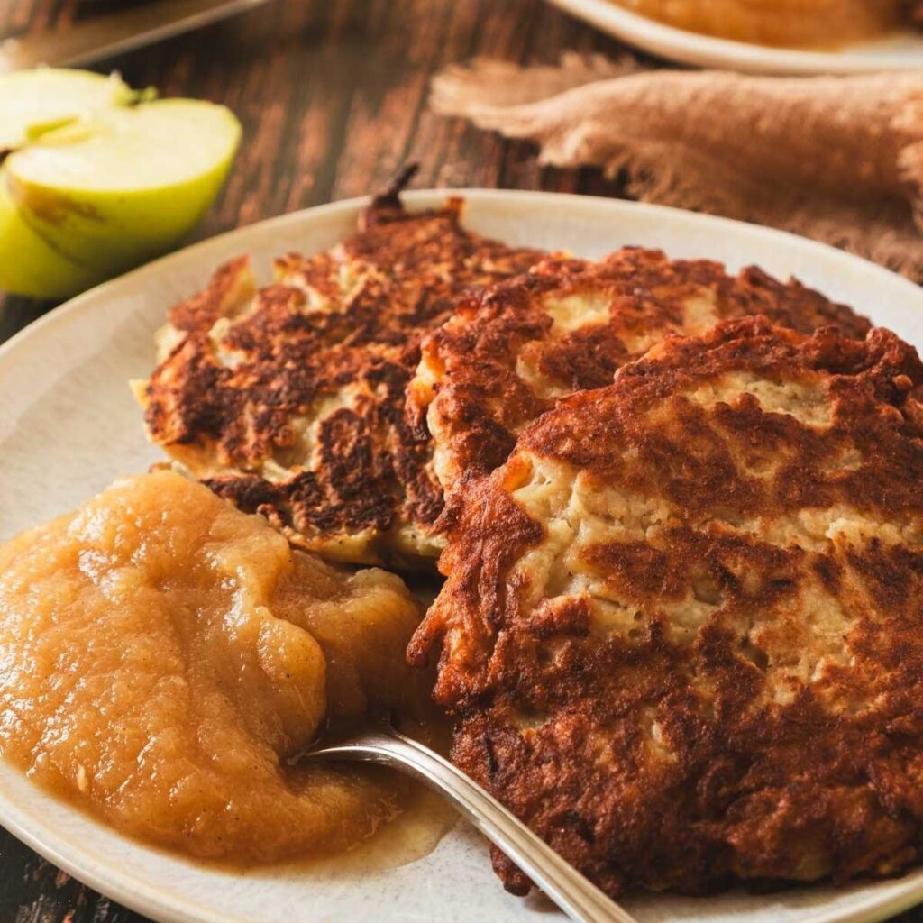 A platter of crispy, golden, round German potato pancakes served with a side of applesauce.