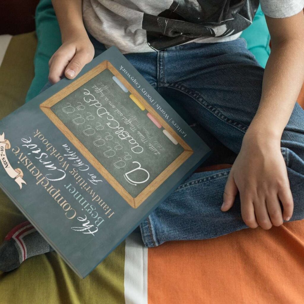 A boy sits cross-legged with a copy of Beginner Cursive by Jana Dziak on his lap.